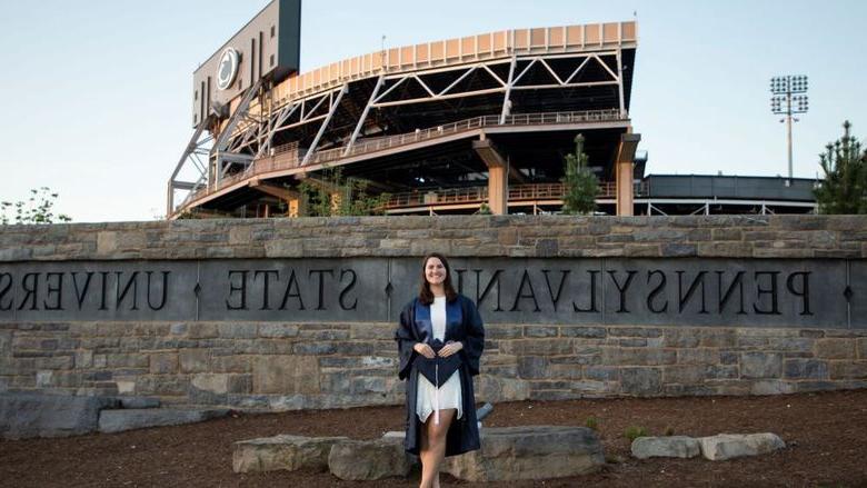 person in cap and gown in front of sports stadium