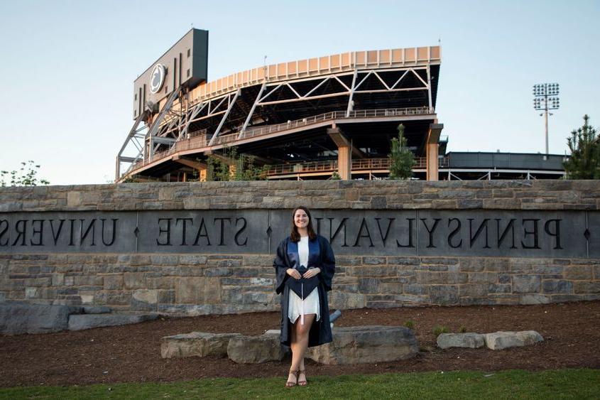 person in cap and gown in front of sports stadium